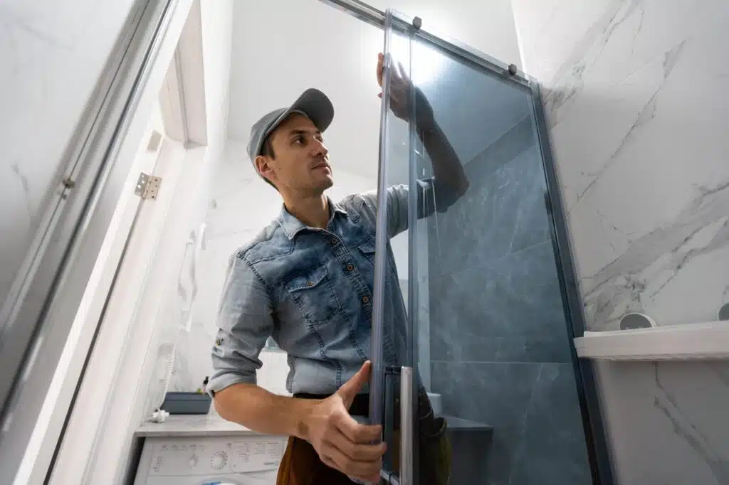 Remodeling bathroom installer placing a shower door into the wall.