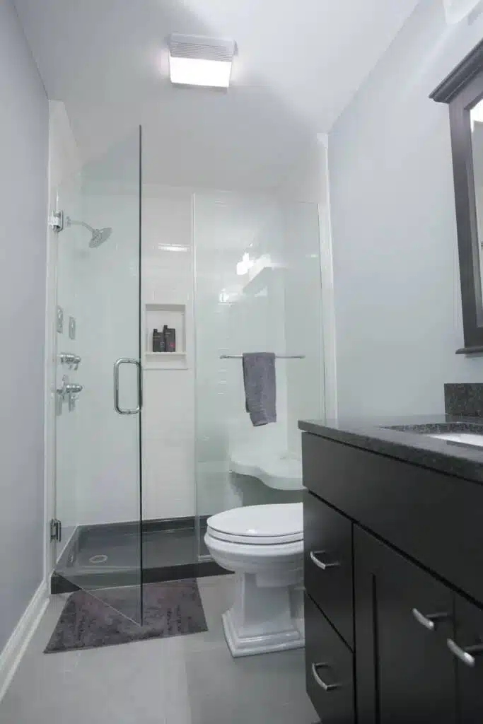 Tiled shower with glass door and modern wooden cabinets and marbeled countertops.