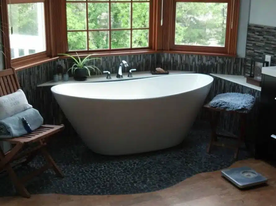 Sloped oval ivory bathtub in exotic, modern bathroom with plants, black carpet, and wood framed windows.
