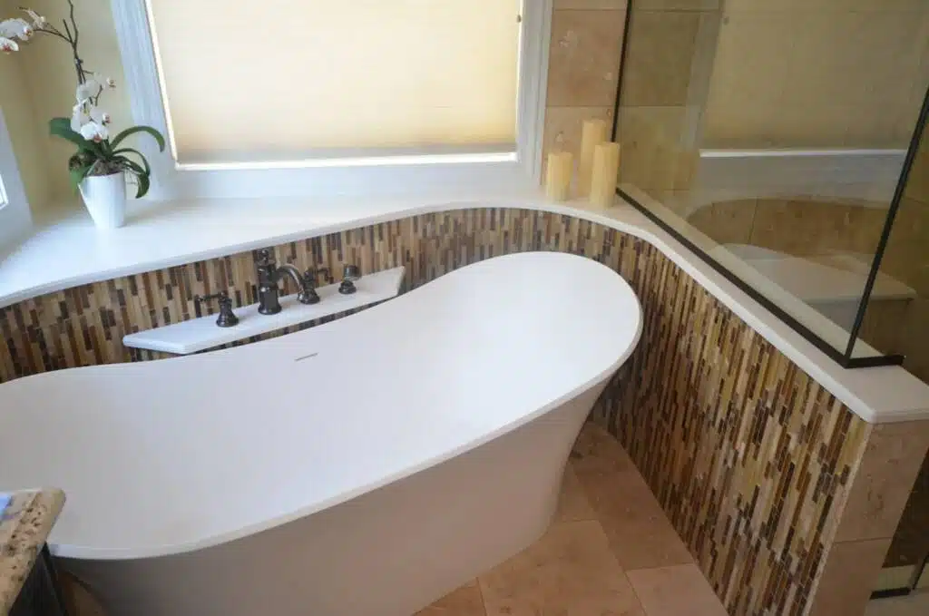 Sloped ivory bathtub in modern and clean bathroom with tiled floors and abstract tiled shelf shaped to suit the natural curve of the tub.