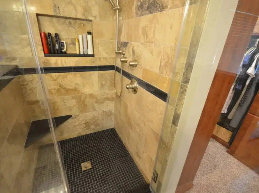 Brown, tan, and grey marbled shower with storage shelf and corner seat.
