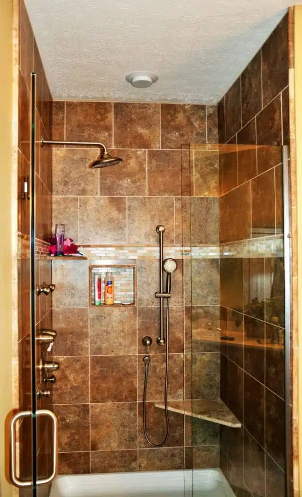Warm brown tiled shower with built-in storage shelf and rainfall shower head.