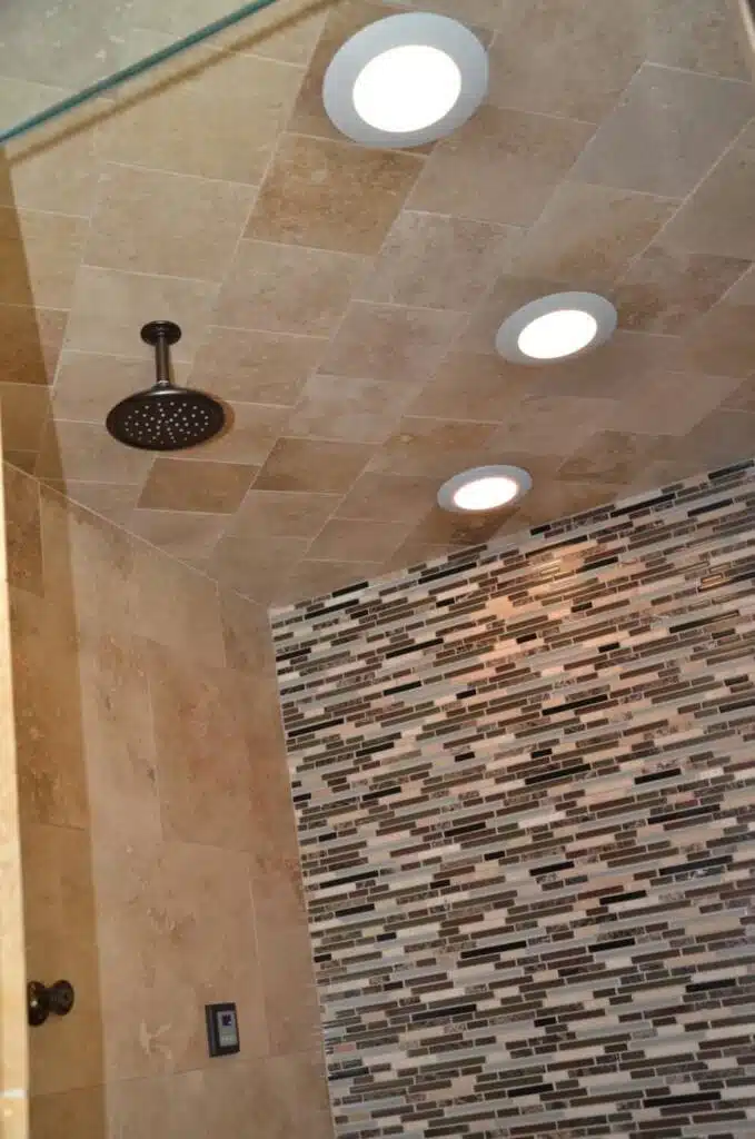 Rainfall shower accessory attached the the ceiling above a warm color tiled shower.
