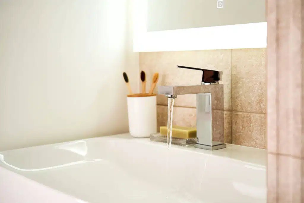 A beautiful white marbled sink with toothbrushes and water running from the faucet.