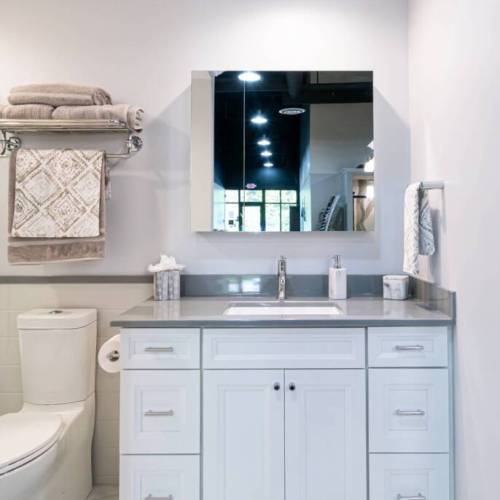 Brightly lit bathroom with large, unframed modern mirror and white cabinets.